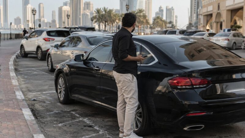 هاتف بيد سائق بجانب سيارة في موقف عام بالشارقة لإعداد رسالة إلى رقم مواقف الشارقة